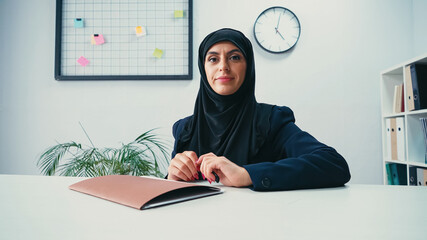 Muslim businesswoman in hijab sitting at desk with folder