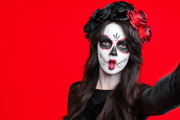 Girl with creative sugar skull makeup with a wreath of flowers on head, wide isolated on red background. Holiday concept Dia De Los Muertos  on poster for Halloween party or La Calavera Catrina.