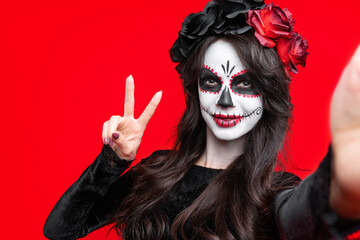 Girl with creative sugar skull makeup with a wreath of flowers on head, wide isolated on red background. Holiday concept Dia De Los Muertos  on poster for Halloween party or La Calavera Catrina.