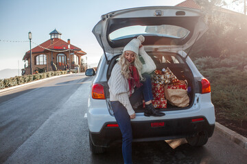 The girl is smiling and sit in the trunk of the car with x-mas boxes. the New Year's mood....