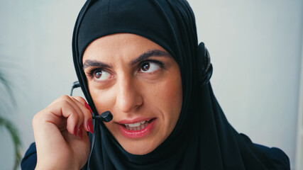 Muslim woman in hijab using headset and talking in call center