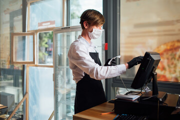 A waiter in a mask places an order on a computer. Precautions during quarantine in a cafe.