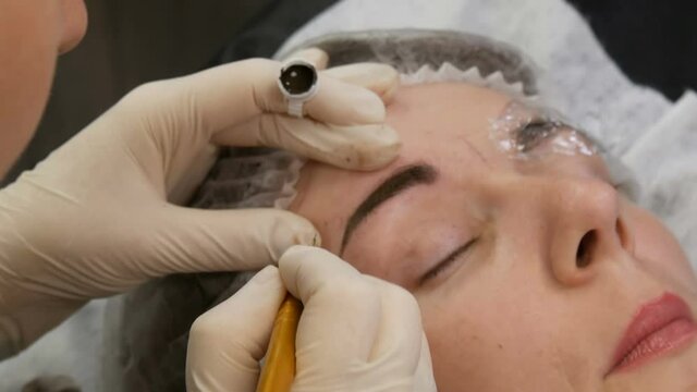 Manual technique of Microblading, master applies a special dark pigment with special pen for coloring eyebrows, permanent makeup, tattooing in beauty parlor