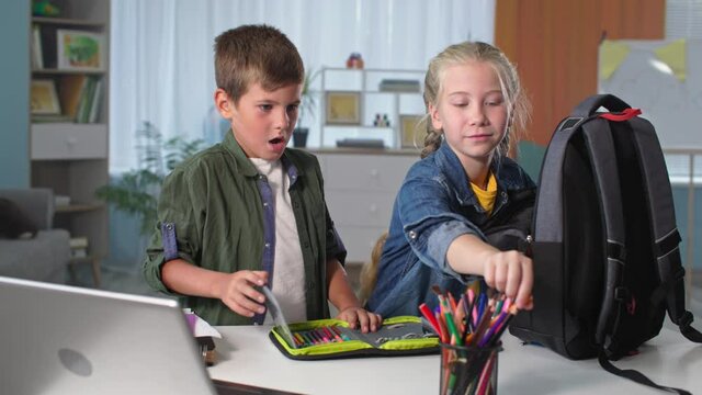 education, children packing schoolbag with school supplies, happy boy and girl with plaster cast have fun at home
