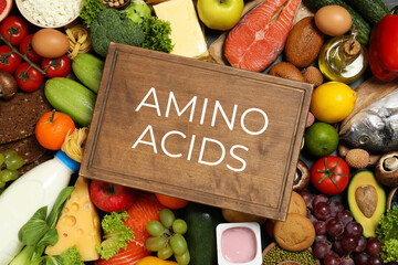 Wooden board with text AMINO ACIDS among different products, top view