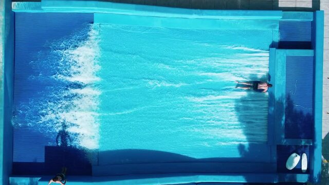 Flowboarding on a surfing machine. Guys rides a surfboards on an artificial wave in wave pool machine. Vacation entertainment in pool built for surfing and boogey board.