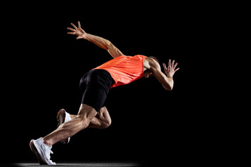 Full-length side view portrait of young male professional athlete running, training isolated over black studio background