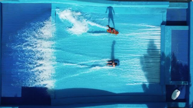 Flowboarding on a surfing machine. Guys rides a surfboards on an artificial wave in wave pool machine. Vacation entertainment in pool built for surfing and boogey board.	
