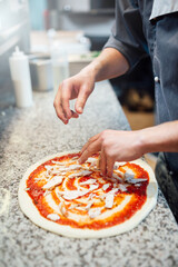 The cook pours the ingredients for the pizza on the dough with sauce. Catering kitchen work.