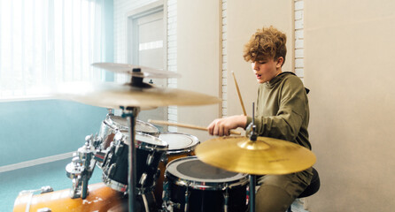 Young teen boy plays drums vigorously in the studio.