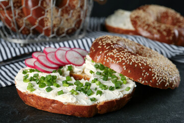 Delicious bagel with cream cheese, radish and green onion on black table, closeup