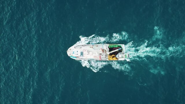 Moving fishing motor boat at the sea. Large fishing ship equipped with nets and a trawler sails through the azure water. Aerial Top View.
