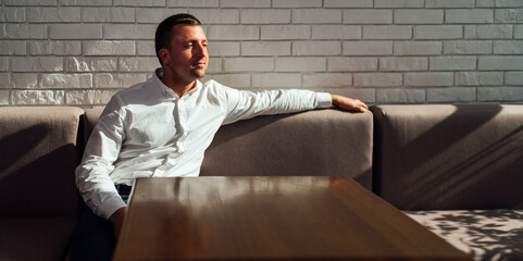 A man in a white shirt sits at an empty table in restaurant.
