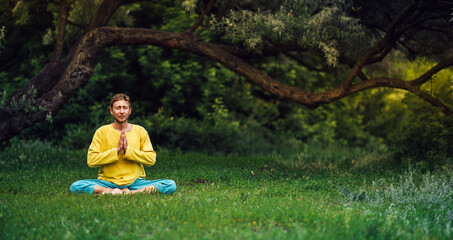 Man sitting in lotus position with arms folded in the namaste gesture. Practicing yoga in the...