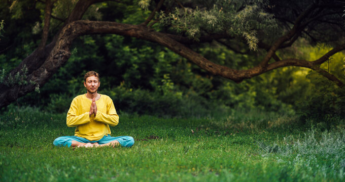 Man sitting in lotus position with arms folded in the namaste gesture. Practicing yoga in the nature.