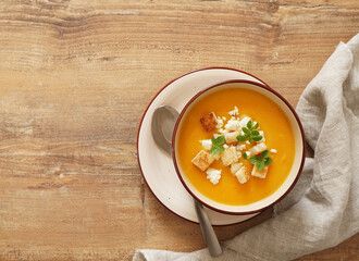 carrot puree soup with cheese and oregano on a wooden table