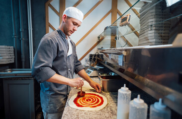 Cook spreads tomato sauce on pizza dough . Catering kitchen work.