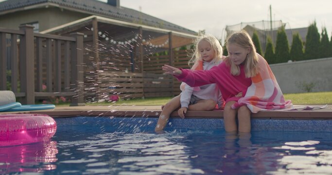 Portrait of happy sisters wrapped in towel sitting near swimming pool