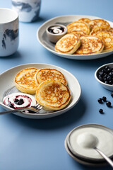 Cottage cheesecakes with sour cream and blueberry jam in a bowl on a blue background. Traditional Russian syrniki. Breakfast concept. 