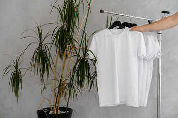 Male hand holds hanger with blank white t-shirt