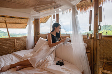 Young asian woman resting and reading a book on the bed in thatched hut among the mountain on...
