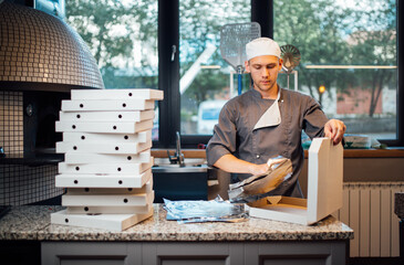 Pizzeria worker folds foil into pizza box. Catering kitchen work. - obrazy, fototapety, plakaty