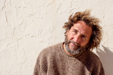 middle-aged man with youthful and carefree attitude is looking at the smiling camera, he has curly hair and wears a sweater