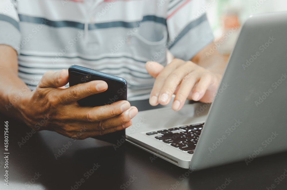 Poster man hand using smart phoneand laptop on table at home, searching information browsing the internet o
