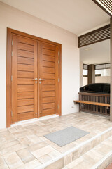 Exterior of a house with wooden door and gray tiled floor. Dark gray doormat on gray tiled floor.