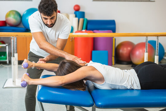 Woman doing shoulder stabilization exercises with small weights, with a help of the male physiotherapist