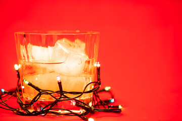 Glass of whiskey with christmas lights on red background christmas drink concept