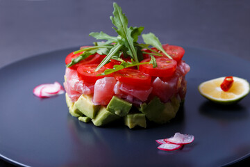 Fresh tuna tartare with avocado, arugula, cherry tomatoes, radish, chili and lime. Traditional cold appetizer of French cuisine. Close-up, selective focus.