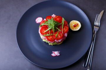 Fresh tuna tartare with avocado, arugula, cherry tomatoes, radish, chili and lime. Traditional cold appetizer of French cuisine. Close-up, selective focus, top view.