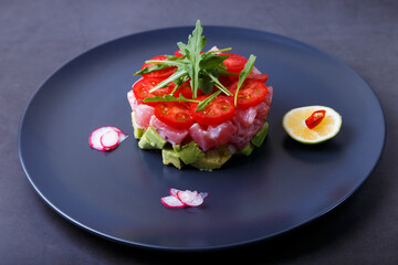 Fresh tuna tartare with avocado, arugula, cherry tomatoes, radish, chili and lime. Traditional cold appetizer of French cuisine. Close-up, selective focus.