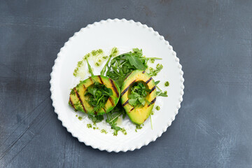 Fried avocado and greens in a plate on a gray background.