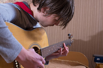 A young man plays the guitar. Close-up photo.