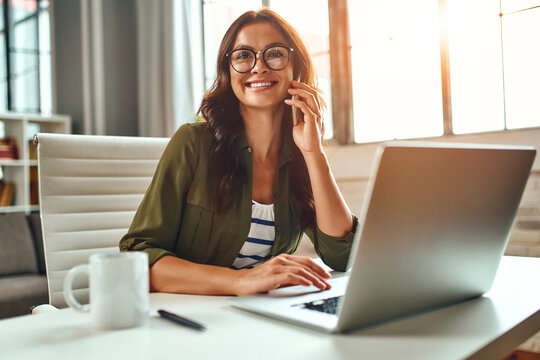 Business woman working at a laptop while sitting at a table at home and talking on the phone. Freelance, work from home.