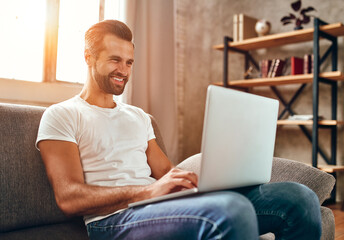 A man is sitting on the couch with a laptop on his lap. Businessman works online from home. Freelance, communication, online shopping.