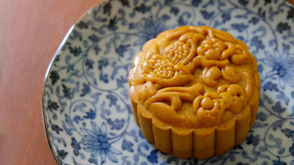 Close up of a brown mooncake with beautiful pattern, placed on a blue plate. Mooncake is a Chinese pastry traditionally eaten during the Mid-Autumn Festival.