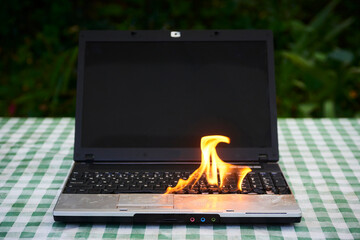 Laptop burning in flames on a desk, fire hazard. losing valuable data. Faulty battery failure....
