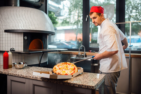 The cook puts the pizza on the spatula in a box. Catering kitchen work.