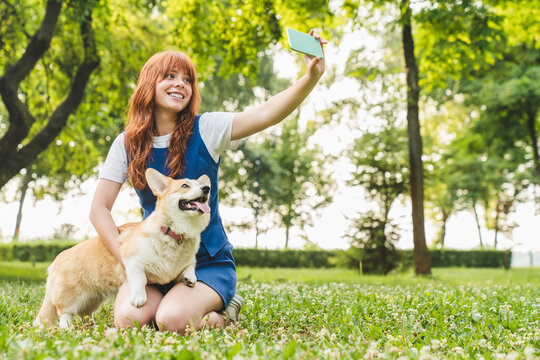 Owner female woman young teenager girl taking selfie photo with her dog welsh corgi pet together on green lawn grass while playing walking in park forest outdoors.