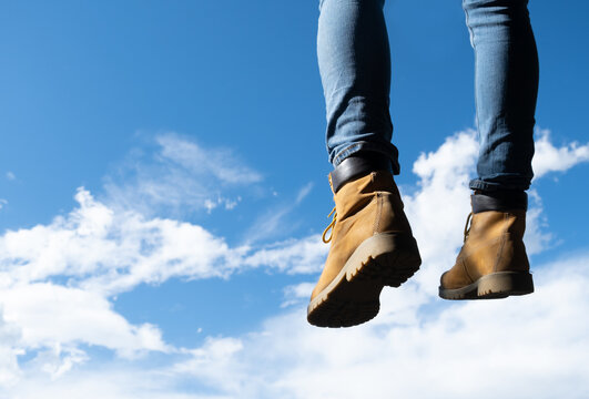 Hanging feet with mountain boots, sky in the background, beautiful nature scenario