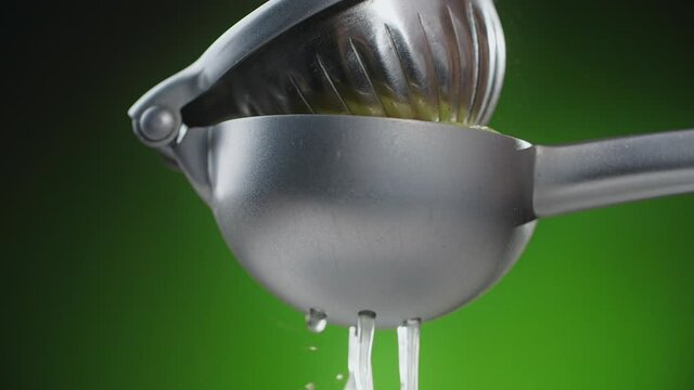 Squeezing the the lemon juice in juicer in slow motion 240fps on the green background, squeezer in action, drops of juice, Full HD Prores HQ