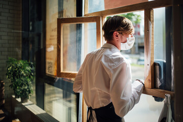 The masked waiter stands near the takeaway window. Precautions during quarantine in a cafe.