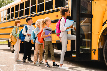 Schoolchildren kids pupils group of mixed-race classmates boarding school bus before going to...