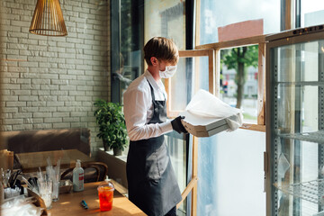 Masked waiter gives a takeaway pizza order. Precautions during quarantine in a cafe.
