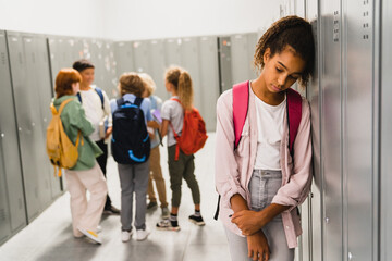 Lonely sad african-american schoolgirl crying while all her classmates ignoring her. Social exclusion problem. Bullying at school concept. Racism problem - obrazy, fototapety, plakaty