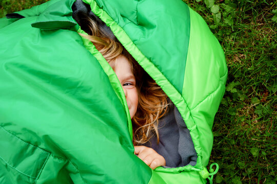 Preschool little girl in sleeping bag camping. Outdoors activity with children in summer. Fun and adventure camp, family and friends vacations or weekend trip. Portrait of child with flashlight.