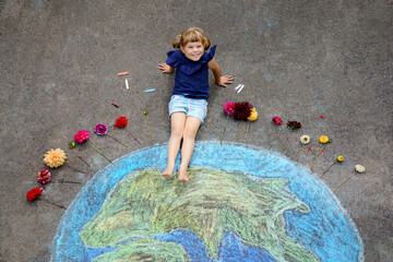 Little preschool girl with flowers and earth globe painting with colorful chalks on ground. Positive toddler child. Happy earth day concept. Creation of children for saving world, environment and